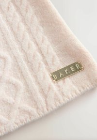 Gaiša rozā adīta auduma ar teksturētām kabelis rakstiem; iekļauj zelta metāla uzlīmi ar gravējumu "BAKER". Mīksta, pūkaina tekstūra.