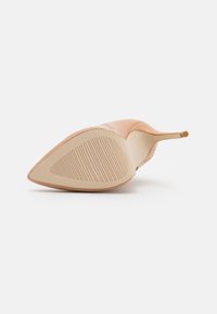 Nude-lackleder-Pumps mit spitzem Zeh und glatter Oberfläche. Die Sohle ist beige mit einem gerillten Muster für besseren Halt.