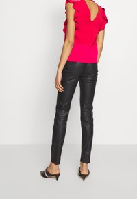 Fuchsiový top s volánkovými rukávy a výstřihem na zádech, v kombinaci s přiléhavými černými koženými kalhotami a černými botami na nízkém podpatku s akcenty.