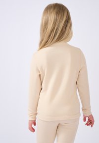Beige geribbelde langemouwen shirt met een ronde halslijn. De stof lijkt zacht, is goed aansluitend bij de taille, met zichtbare naden langs de randen.