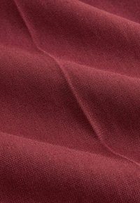 Tissu rouge foncé avec une fine texture tissée, présenté en plis doux et en gros plan.