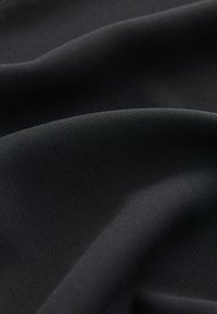 Tessuto nero con una superficie liscia, caratterizzato da sottili motivi a coste, drappeggiato per evidenziare la sua qualità morbida e flessibile.