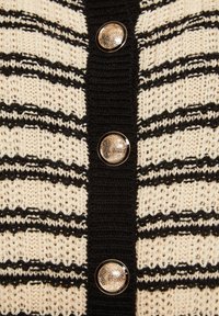 Tissu en tricot crème avec des rayures horizontales noires, doté d'une bordure côtelée noire et de trois boutons ronds texturés dorés au centre.