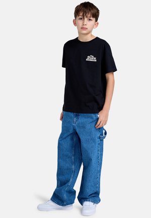 Zwarte katoenen t-shirt met wit logo, gecombineerd met losse blauwe denim jeans en witte sneakers. Simpel ontwerp zonder zichtbare patronen.