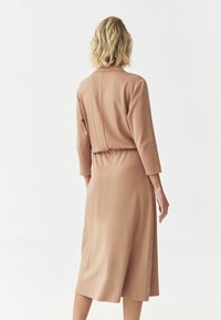 Pitkä, löysä mekko pehmeästä beige materiaalista. Ominaisuuksiin kuuluu pyöreä kaula-aukko, kolme neljäsosapituista hihaa ja joustava vyötärö. Tasainen tekstuuri.