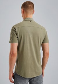 Polo majica kratkih rukava maslinaste boje s kragnom, koja ima suptilan teksturirani uzorak i zaobljeni donji rub.