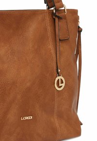 Braune Kunstlederhandtasche mit strukturiertem Finish, goldenen Metallverzierungen und einem Logo-Anhänger. Verfügt über einen Schultergurt und ein offenes Oberdesign.