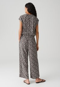 Jumpsuit estampato in bianco e nero con vestibilità morbida, maniche corte e vita elastica. Design a gamba larga e texture in tessuto morbido.