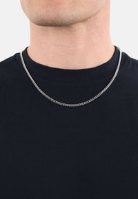 Collana a catena argentata appoggiata su una t-shirt nera, caratterizzata da un design a maglie rotonde e una superficie liscia e lucida, che mette in evidenza la sua finitura metallica.