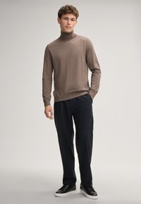 Brauner Rollkragenpullover aus weichem Stoff, kombiniert mit schwarzen Hosen und schwarzen Sneakers, mit lässiger Passform und minimalistischem Design.