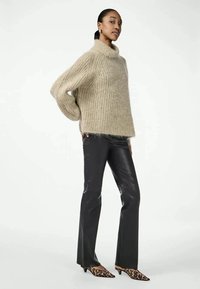 Sweater de malha oversized bege com um decote alto, combinado com calças pretas de boca de sino e sapatos de salto com padrão de leopardo, exibindo um tecido texturizado.