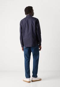 Navy button-up shirt with contrasting white stitching, paired with blue denim jeans and white sneakers. Rear view of the outfit.