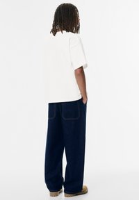 Weißes Baumwoll-T-Shirt mit lockerer Passform, kombiniert mit dunkelblauen weiten Jeans, die über Gesäßtaschen und kontrastierenden Nähten verfügen.