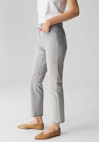 Jeans in denim grigio con un design aderente, vita media e dettagli di cucitura sottili. Abbinati a ballerine beige senza laccio.