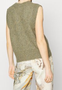 Olijfgroene, mouwloze gebreide sweater met een geribbelde structuur. Heeft een ronde halslijn en een iets losse pasvorm.