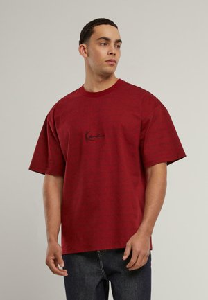 Camiseta roja de manga corta con un patrón sutil y un logo negro centrado. Cuello redondo, corte relajado, textura suave similar al algodón.