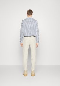 Pruhované modro-bílé tričko s dlouhým rukávem, doplněné o světle béžové kalhoty. Celkový vzhled je dokončen hnědými kotníkovými botami.