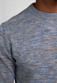 Jersey de punto con una mezcla de texturas en tonos azules y marrones, con un cuello redondo de canalé y mangas largas.