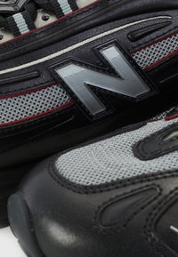 Gros plan sur des baskets New Balance noires et grises montrant un tissu texturé, des détails en cuir et un logo "N" en relief sur le côté.