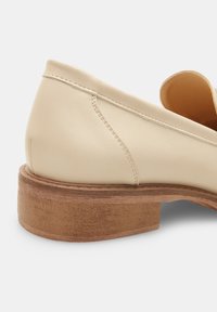Scarpa in pelle beige con punta arrotondata e tacco in legno basso, con cuciture visibili lungo il lato superiore. Texture complessiva liscia.