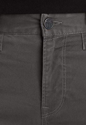 Szare materiałowe spodnie o gładkiej fakturze, z zapięciem na guziki i kontrastowym stębnowaniem wzdłuż przedniej części oraz kieszeni bocznych.