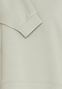 Detailní záběr béžového dlouhého rukávu se sukýnkovým manžetem a viditelným švem na měkké látce.