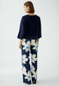 Marineblauer Pullover mit Dreiviertelärmeln; weit geschnittene Hose mit großen weißen und blauen Blumenmustern auf dunklem Hintergrund.