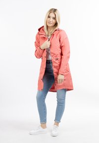 Jachetă impermeabilă corai cu glugă, nasturi prin presare și manșete elastice. Asortată cu blugi deschiși la culoare și adidași albi. Textură fină.