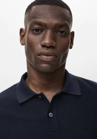 Polo de color navy con tejido texturizado, con un collar clásico y tapeta de dos botones. El corte es ajustado al cuerpo.