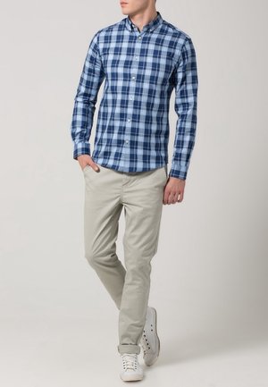 Koszula w niebiesko-białą kratę z kołnierzykiem na guziki, zestawiona z jasnobeżowymi chinosami i białymi trampkami. Gładka tkanina o dopasowanym kroju.
