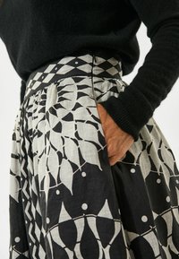 Plisirana krila z kontrastnim črno-belem geometrijskem vzorcu, izdelana iz lahkotnega blaga z teksturirano površino.