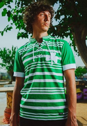 Groen en witte gestreepte short-sleeve shirt met een vetersluiting en een groot klavertje vier ontwerp op de voorkant. Gemaakt van katoenen stof.