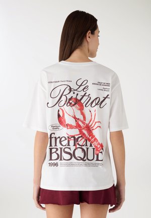 T-shirt bianca a maniche corte con una grande grafica di un'aragosta rossa e testo in nero e rosso. Il design include "Le Bistrot" e "French Bisque."