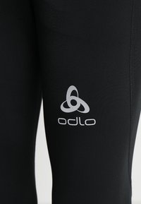 Černé legíny vyrobené z elastického materiálu mají stříbrné logo Odlo na dolní části nohy, s hladkým texturem a přiléhavým střihem.