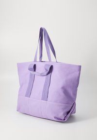 Lila Baumwoll-Tote-Tasche mit zwei oberen Griffen, einem geräumigen Hauptfach und einer Fronttasche. Einfaches, langlebiges Design mit sichtbaren Nähten.