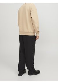 Felpa beige con una vestibilità rilassata, polsini e orlo a coste. Abbinata a pantaloni neri, caratterizzati da una texture liscia e una siluetta casual.