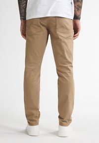 Pantalones de algodón color beige con corte ajustado y bolsillos traseros que presentan un diseño de costura único, combinados con zapatillas bajas blancas.