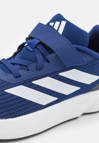 Zapatos deportivos para hombre con parte superior de malla azul, acentos de rayas blancas, cordones planos y una correa de Velcro, con una entresuela blanca.