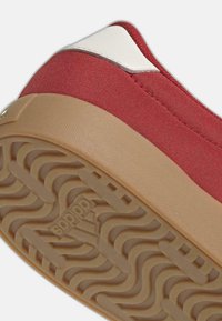 Röd kanvassko med vit accent, med en texturerad gummisula i beige med ett vågmönster och präglad logotypdetalj.