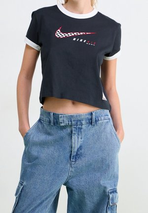 Zwarte cropped t-shirt met witte manchetten, voorzien van een rood en geruit Nike-logo. Gecombineerd met losse blauwe denim cargobroek.