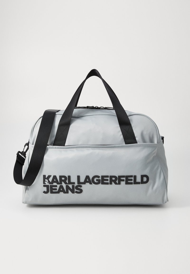 Grå nylon duffelbag med svarte detaljer; har doble topphåndtak, en avtakbar skulderrem, og logo tekst "KARL LAGERFELD JEANS".