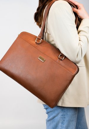 Sac tote en cuir marron avec une texture lisse, fermeture à glissière et détails en métal doré. Dispose de deux poignées robustes pour le transport.