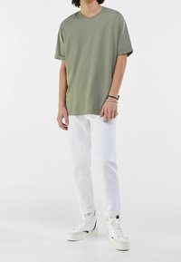 Camiseta de manga corta en verde oliva, de corte relajado, combinada con jeans de mezclilla blancos y zapatillas altas blancas con detalles negros.