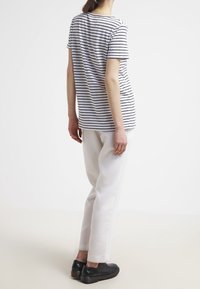Camiseta de algodón a rayas con mangas cortas, combinada con pantalones blancos y calzado negro, vista desde la parte de atrás contra un fondo liso.