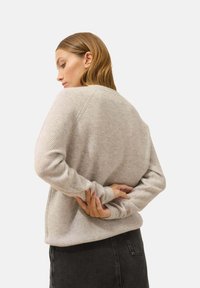 Hellgrauer, gerippter Strickpullover mit langen Ärmeln, Rundhalsausschnitt und lässiger Passform, kombiniert mit dunklen Jeans. Keine sichtbaren Muster oder Akzente.