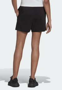 Mustat puuvillashortsit yksinkertaisella suunnittelulla, sivutaskut ja rento istuvuus, yhdistettynä mustiin urheilukengiin.