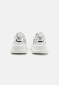 Weiße Sportschuhe mit einem strukturierten silbernen Mesh-Obermaterial, ausgestattet mit einem gepolsterten Kragen, einem Ziehriemen und einer dicken weißen Gummisohle.