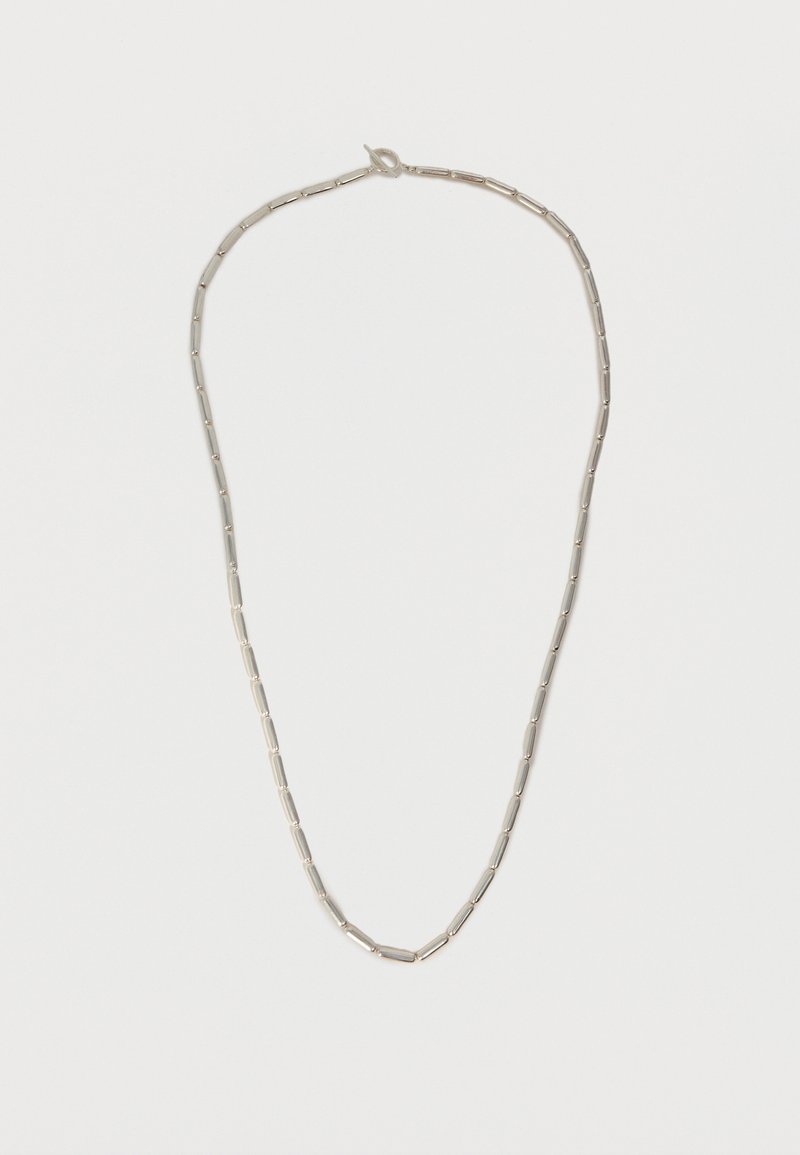 Ασημένιο κολιέ με ομοιόμορφα διάσπαρτες επιμηκείς κυλινδρικές χάντρες και μικρό κούμπωμα γάντζου σε απλό λευκό φόντο.