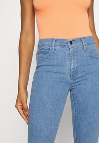 Vaqueros de tiro alto en azul claro, confeccionados en denim, que presentan un diseño de cinco bolsillos y un sutil efecto de desgastado cerca de las caderas.