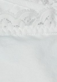 Tissu en coton blanc avec une texture lisse, présentant une bordure en dentelle décorative en haut avec des bords festonnés et des motifs complexes.